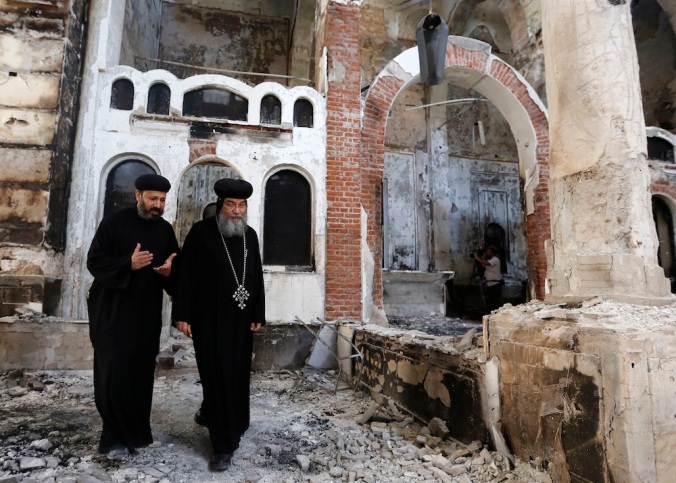 Bishop-General Macarius, a Coptic Orthodox leader, walks around the burnt and damaged Evangelical Church in Minya governorate